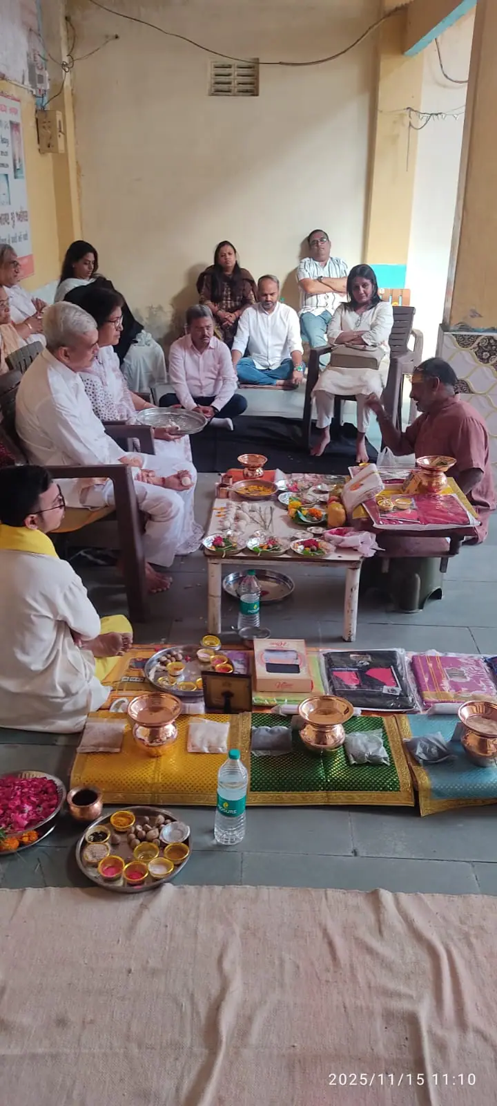 શ્રાદ્ધ દરમિયાન વિધિ હૉલમાં બેઠેલો પરિવાર, નીચા બાજઠ પર પૂજાની સામગ્રી ગોઠવેલી છે