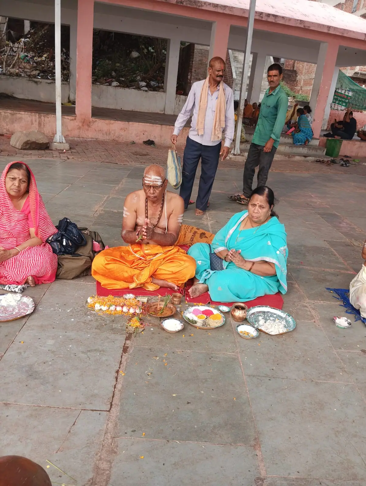 A woman in a blue sari performing a ritual with a purohit on the stone floor of the Bindu Sarovar complex